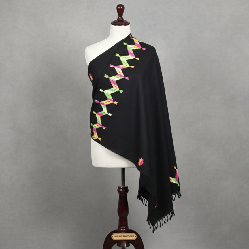 Black shawl with colorful patterns draped over a mannequin against a gray background