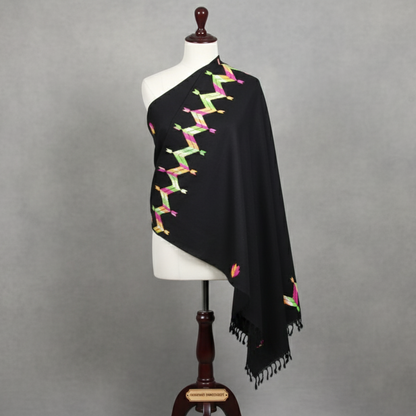Black shawl with colorful patterns draped over a mannequin against a gray background