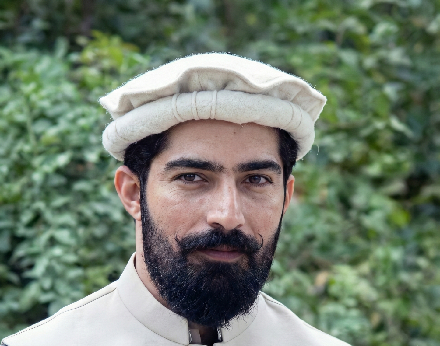 Man wearing a traditional white cap and outfit with a blurred green background