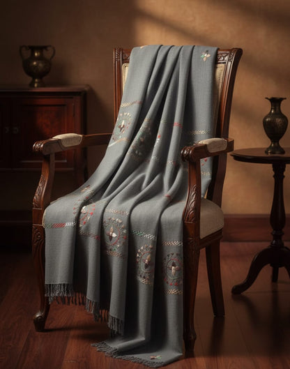 Gray embroidered blanket draped over a wooden chair in a warm-toned room.
